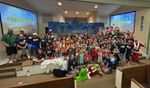 a large group of children and adults posing in front of a Christmas-themed background