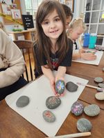 child posing with painted rocks on craft table