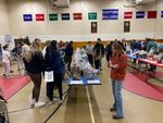 people at a silent auction, with items on tables in a school gym