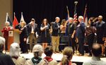 people standing for the National Anthem on stage in front of flags