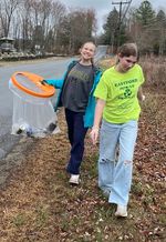 two people with a trashbag by a road and cemetery