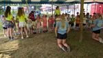 children lined up under a tent, supervised by several adults