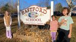 Three children posing in front of the school sign