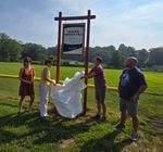 people pulling a sheet off of a tall sign in front of a baseball field