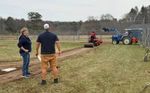 two people watching a tractor compact dirt with a roller