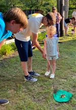 two adults bending over watching a child make a frog jump with a feather