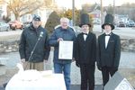 Two boys in top hats receiving an award from two men, with a duck on the table