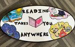 A sign that says "reading takes you anywhere", with drawings of a sandy beach, outer space, books and a mortarboard hat, and scientific and medical equipment
