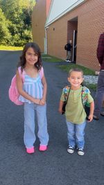 two children posing in front of a brick school building