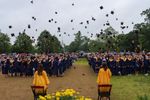 a large group of high-school students in blue gowns with orange collars throw their caps