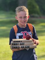 a child posing with a stack of books and an apple