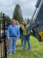 four men with an excavator next to a gate