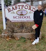 a student poses the school sign with the new drawing in the middle